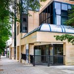 Modern building with glass facade on leafy street.