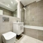 Modern bathroom with beige tiles and white fixtures.