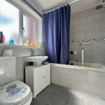 Modern bathroom with grey tiles and blue curtain.
