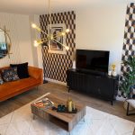 Modern living room with geometric wallpaper and orange sofa.