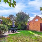 Sunny garden with patio and brick building.