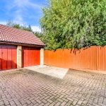 Brick garage and driveway with wooden fence and trees.