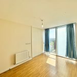 Sunlit empty room with wooden floor, window view.