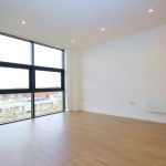 Spacious empty room with large window and wooden floor.