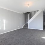 Grey carpeted room with stairs and light.
