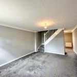 Empty grey carpeted living room with staircase.