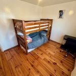 Wooden bunk bed in small room with desk.