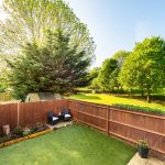 Sunny garden with trees and patio chairs.