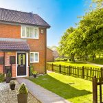 Sunny suburban house with garden and picket fence.