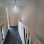 Carpeted hallway with white staircase and light fixture.
