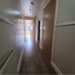 Narrow hallway with wooden floor and open door.