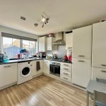 Modern kitchen with white cabinets and wood flooring.