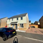 Modern detached house with parked car in sunny street.