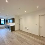 Modern empty kitchen with wooden flooring and white walls.