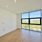 Bright empty room with large window and wooden floor.