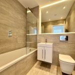 Modern bathroom with bathtub, toilet, and large mirror.