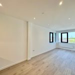 Spacious unfurnished room with large windows and wooden flooring.