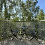 Small balcony with table and chairs, leafy view.
