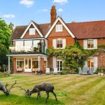 Traditional English house with garden and deer sculptures.