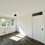 Bright empty room with window and wooden floor.