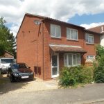 Two-storey brick house with cars parked outside.