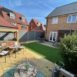 Sunny garden with patio furniture and brick house.