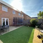 Sunny backyard with patio, trampoline, and artificial grass.