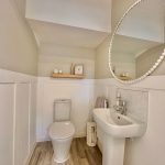 Modern bathroom with mirror and wooden shelf.