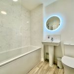 Modern bathroom with bathtub and illuminated mirror.