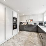 Modern kitchen with white cabinets and herringbone floor.