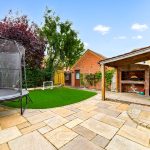 Garden with trampoline, patio, brick shed, trees.