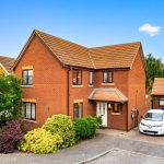 Brick house with driveway and cars in suburban street.