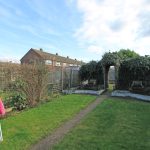 Suburban garden with ivy-covered archway and pink umbrella.