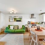 Modern open-plan living room and kitchen with green sofa.
