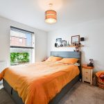 Bright bedroom with orange duvet and window view.