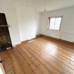 Empty room with wooden floorboards and small windows.