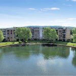 Lakeside apartment complex with trees and blue sky.