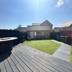 Sunny garden with patio, lawn, shed, and bins.