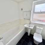 Modern white bathroom with tub and black tile floor.