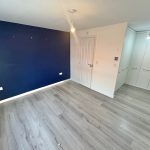 Empty room with blue accent wall and wooden floor.