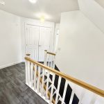 Bright hallway with wooden banister and white doors.
