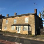 Stone house on roadside with blue sky.
