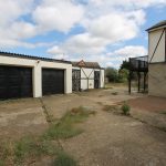 Rural property with garages and overgrown courtyard.