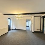 Empty room with chandelier, white walls, carpeted floor.
