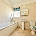 Modern beige tiled bathroom with bathtub and toilet.
