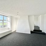 Spacious bright room with large window and carpet.