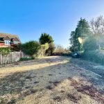 Sunny driveway beside a brick house and trees.