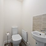 Minimalist toilet with sink, radiator, and beige tiles.