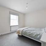Minimalist bedroom with grey carpet and white walls.