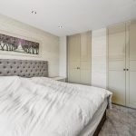 Modern bedroom with grey headboard and wardrobes.